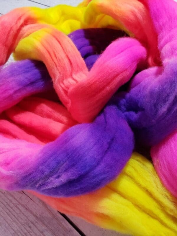 A pile of Disco Date ~ 100g Hand-Dyed Luxury Combed Top Fiber on a wooden table.