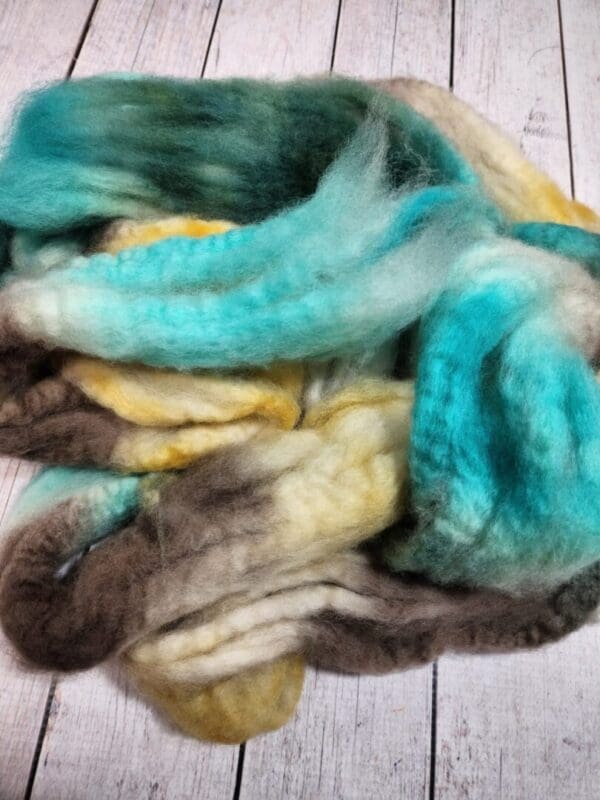 A pile of Disco Date ~ 100g Hand-Dyed Luxury Combed Top Fiber on a wooden floor.