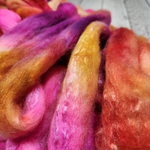 A pile of Disco Date ~ 100g Hand-Dyed Luxury Combed Top Fiber on a wooden table.