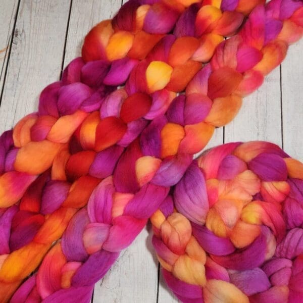 A skein of orange and pink roving on a wooden table.
