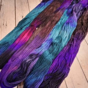 Skeins of purple, blue, and green yarn on a wooden floor.