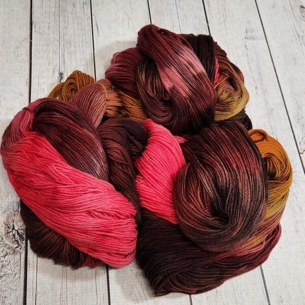 Skeins of red, brown and orange yarn on a wooden floor.