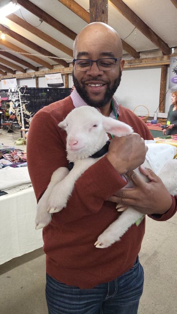received_895541845433580 A man holding a baby lamb.
